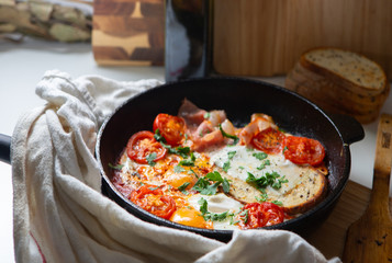 Fried eggs with bacon, toast and tomatoes in a pan