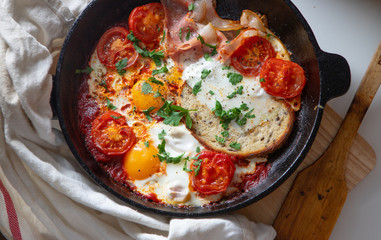 Fried eggs with bacon, toast and tomatoes in a pan