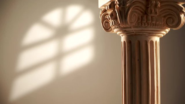 Single ancient corinthian column rotating slowly on bright wall background with window light effect