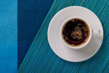 Top view of a black coffee cup on blue bamboo mat and fabric background