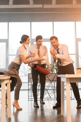 Obraz premium terrified businessman holding extinguisher near yelling coworkers looking at smartphone in office