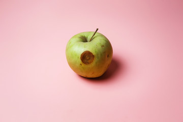  rotten green apple on a pink background. concept of spoiled food and junk food
