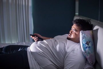 Asleep obese man in bedroom during watches TV