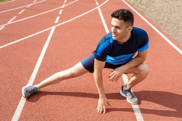 Obraz premium Marathon preparation. Young man on stadium outside stretching on track smiling happy