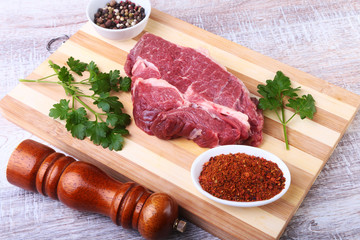 Raw beef steak with spices Leaves of coriander on wooden cutting board. Ready for cooking.