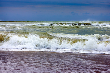 View of storm seascape with sandy beach at cloudy day. Waves in the sea and sand on the beach against stormy sky