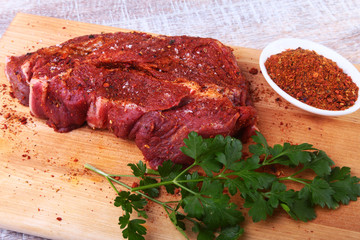 Raw beef steak with spices Leaves of coriander on wooden cutting board. Ready for cooking.