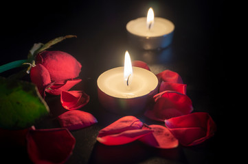 Two tea candles, red rose and rose petals on black