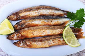 Deep frying small fish capelin and sliced lemon on white plate. Good snack to beer.