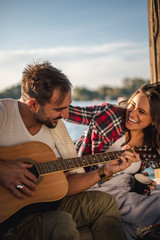 Couple laughing and playing guitar by the river