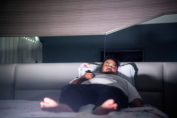 Fat man falls asleep during watches TV on the bed