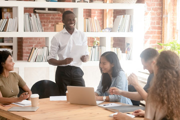 Smiling black leader holding paper report laughing with diverse team