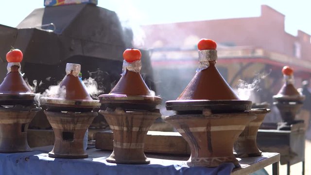 Traditional moroccan Tajine food cooking in Tajine pots on the fire with smoke and tomatoes on top