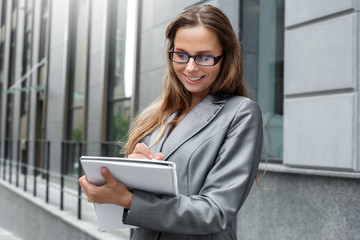 Business woman in eyeglasses standing on the city street taking notes in journal smiling cheerful