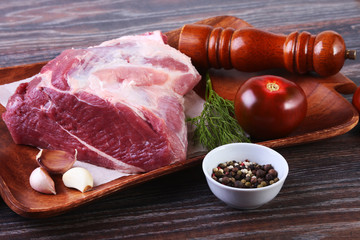 Raw pork steaks on wooden board with herbs, spices, tomatoes and pepper grinder ready for cooking. Selective focus