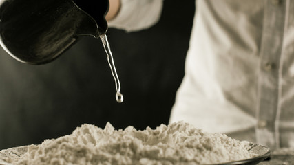 The cook pours water on the flour from the jug in the kitchen