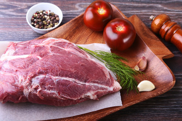Raw pork steaks on wooden board with herbs, spices, tomatoes and pepper grinder ready for cooking. Selective focus