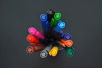 Set of multi-colored bright pens standing in a transparent glass, top view on black background