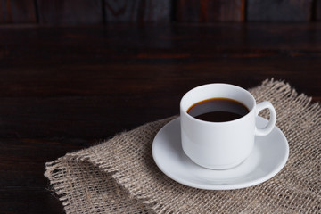 White cup of coffee on linen fabric on the dark vintage background