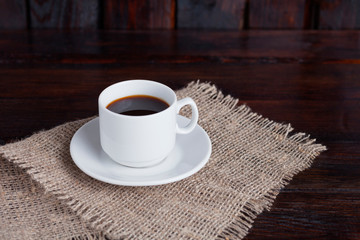 White cup of coffee on linen fabric on the dark vintage background
