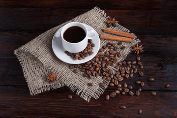 White cup of coffee with coffee grains near on linen fabric on the dark vintage background