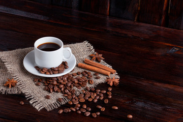 White cup of coffee with coffee grains near on linen fabric on the dark vintage background