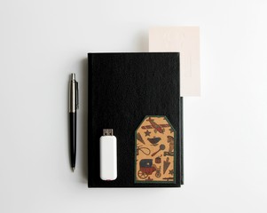 Black diary, pen, white flash drive and a small card are on a white background