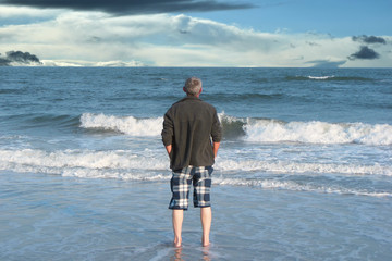 man on the shore of the cold ocean looking into the distance