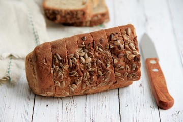 Dark bread is cut into pieces and is on a wooden light background next to it is a knife