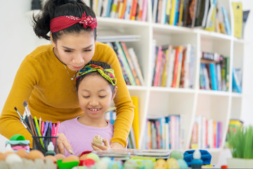 Mother guiding her daughter to paint Easter eggs