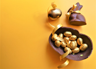 Golden chocolate Easter eggs and chocolate bunny  on a yellow background