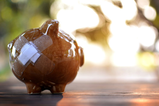 Broken piggy bank on wood plank and tree bokeh background , saving and protecting money concept.