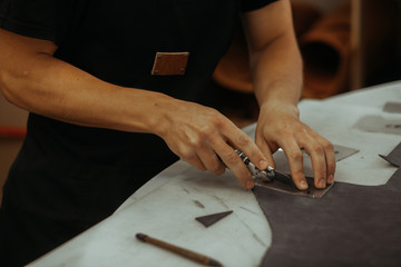 Man holding crafting tool and working. Close up of a master working with leather textile at his workshop using tools. Handmade concept.