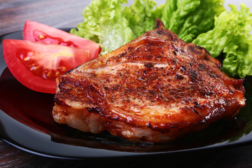 grilled pork chops with tomato, leaves lettuce and ketchup on plate.