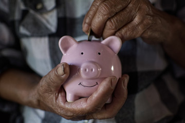 Old hand holding coin dropping to pink piggy bank ,saving and protecting money concept.color of retro style.