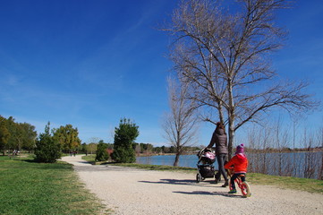 Maman avec poussette et petit enfant en vélo le long du lac