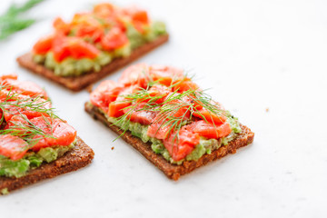 Close-up view of three sandwiches with rye bread, avocado and smoked salmon on a white kitchen table. Copy space.