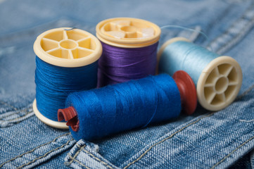 closeup of sewing thread spool bobbin on blue jeans background