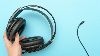 Fototapeta na wymiar Hand keaping black headphones, and a mini-jack cable on blue background. Top view