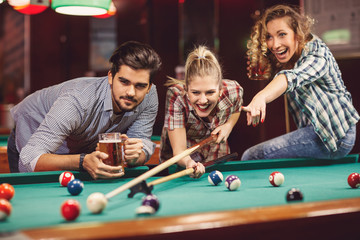 Young adults friends in bar playing billiard.