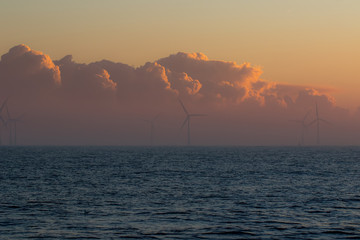 Low bank of misty cloud behind offshore wind turbines. Spiritual landscape.