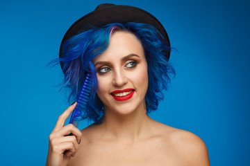 Portrait of a woman with blue hair in a black hat and with a blue hairbrush in her hand