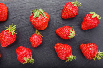 Fresh homemade strawberries on a black slate board, top view.