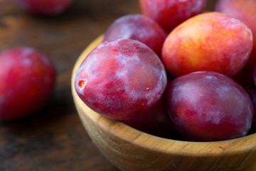 Wooden plate with ripe juicy plums on table.