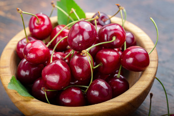 Wooden plate with ripe juicy cherries on table.