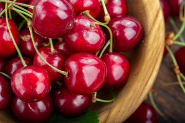 Wooden plate with ripe juicy cherries on table.