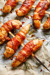 Grilled skewers of chicken tenderloin wrapped with bacon on baking paper, view from above
