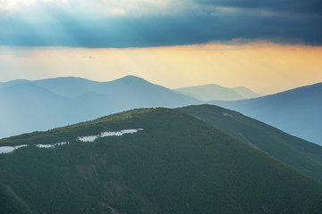 Naklejka premium Dramatic sunset in the spring Ukrainian carpathians with red skies, rays and dark clouds, against the background of mountain ridges covered with alpine pine.