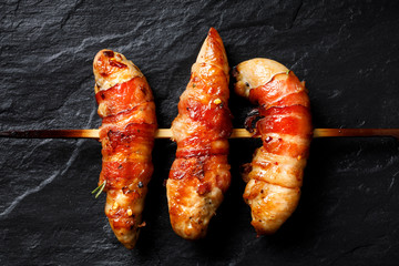Grilled skewers of chicken tenderloin wrapped with bacon on a black background, top view