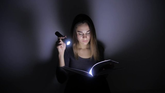 close-up portrait girl is reading a book with a flashlight in a dark room at night. 4k. Motion shooting